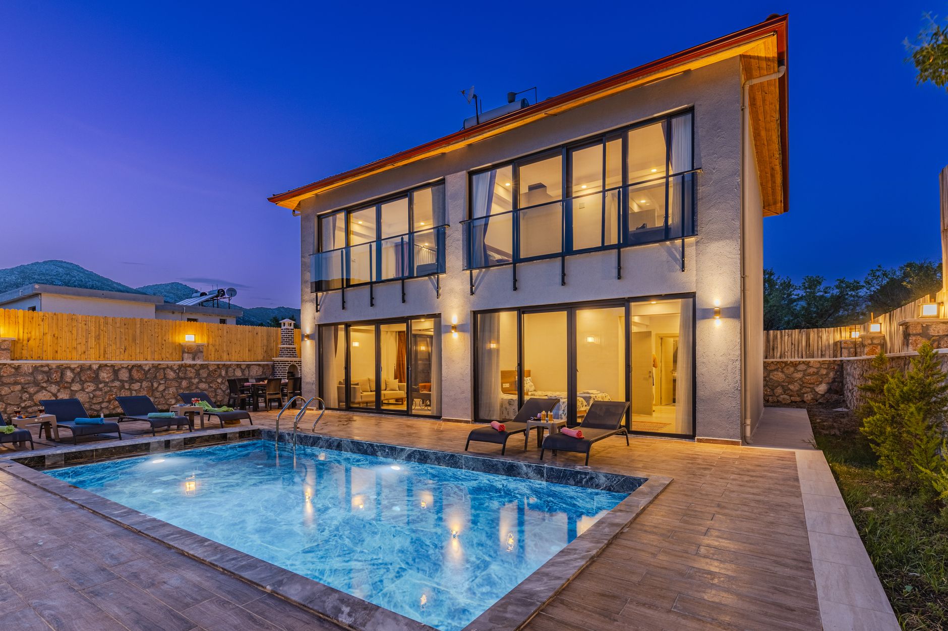 A modern two-storey villa with a lit pool at dusk